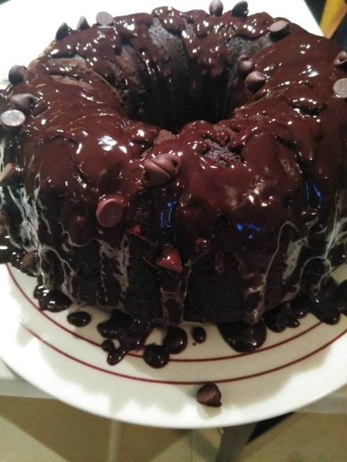 A chocolate bundt cake drizzled with glossy chocolate ganache and topped with chocolate chips.