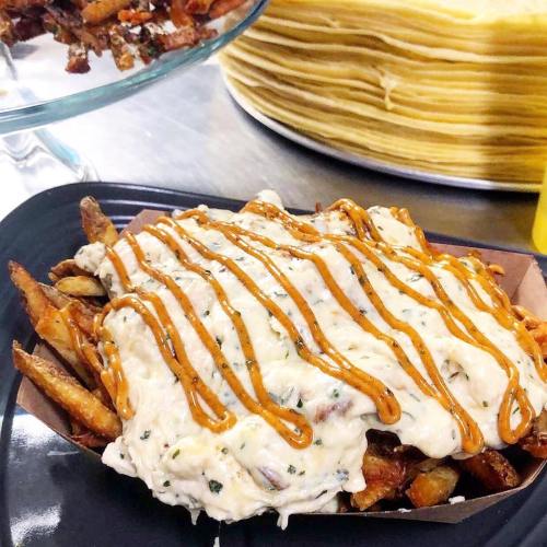 A plate of loaded fries topped with creamy sauce and herbs, served alongside a stack of tortillas.
