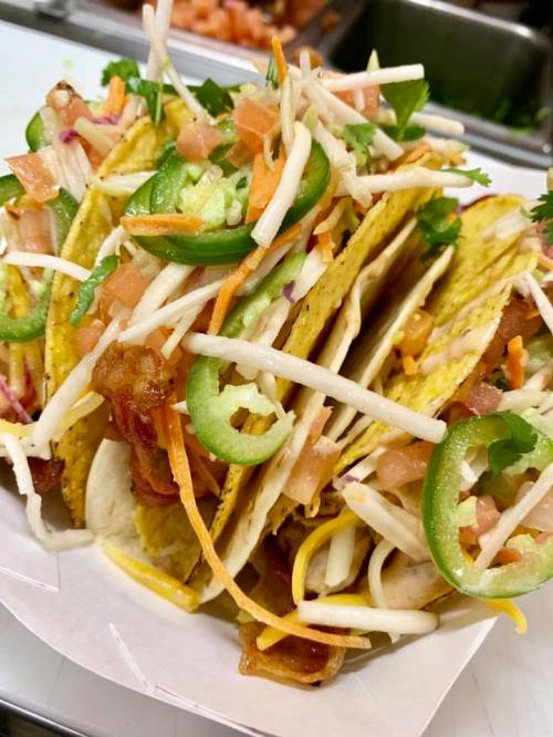 A close-up of three tacos filled with colorful toppings like lettuce, tomatoes, jalapeños, and shredded cheese.