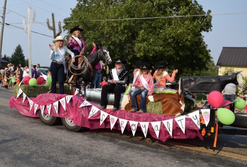 A colorful parade float with people in cowboy attire, a horse, and festive decorations, celebrating a local event.