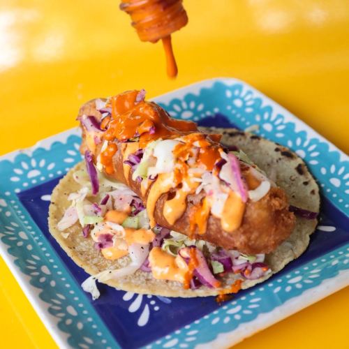 A crispy taco filled with slaw and drizzled with orange sauce, placed on a colorful plate against a bright yellow background.