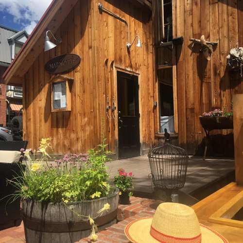 A rustic wooden building with a sign, surrounded by flowers and a straw hat on the ground, under a clear blue sky.