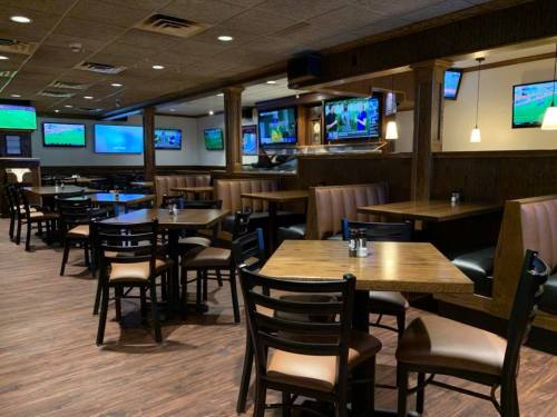 A spacious restaurant interior with wooden tables, chairs, and multiple TVs displaying sports.