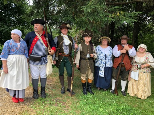 A group of people in historical costumes, representing different eras, standing together outdoors.