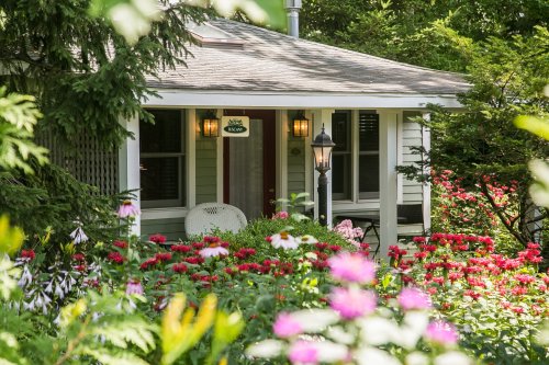 A charming house surrounded by vibrant flowers and greenery, with a welcoming porch and a lamp post.