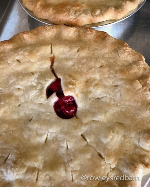 Two freshly baked cherry pies with golden crusts, one showing a small crack with cherry filling peeking through.