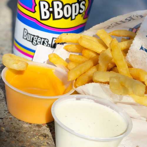 A colorful cup from B-Bop's next to a serving of fries and two dipping sauces on a table.