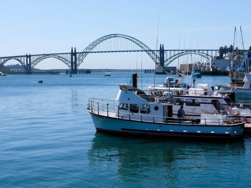 A boat floats in calm water with a bridge in the background under a clear blue sky.