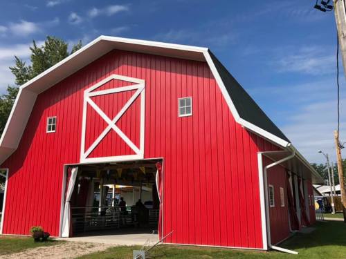 A bright red barn with white trim and windows, set against a blue sky with a few clouds.