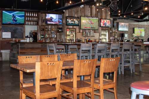 A rustic bar with wooden furniture, multiple TVs showing sports, and a well-stocked bar in a lively atmosphere.