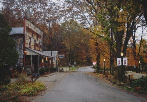 A rustic building with autumn foliage lining a quiet road, featuring warm lights and a welcoming atmosphere.