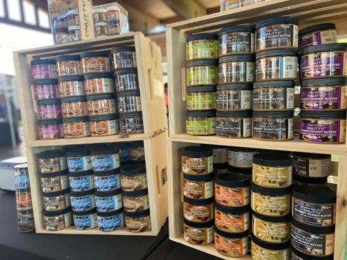 Shelves displaying various jars of peanut butter in colorful packaging, arranged in wooden crates at a market.
