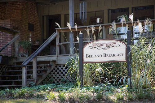 Sign for a bed and breakfast in a historic district, with a porch and greenery in the foreground.