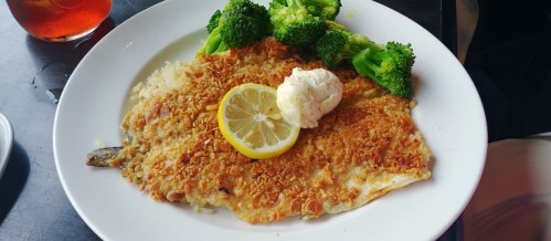 A plate of crispy fish fillet topped with a lemon slice and butter, served with steamed broccoli.