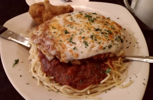 A plate of spaghetti topped with marinara sauce, melted cheese, and a piece of fried chicken on the side.