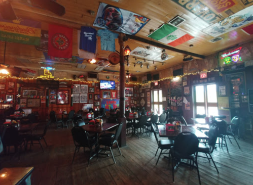 Interior of a rustic bar with wooden floors, tables, and walls adorned with flags and memorabilia.