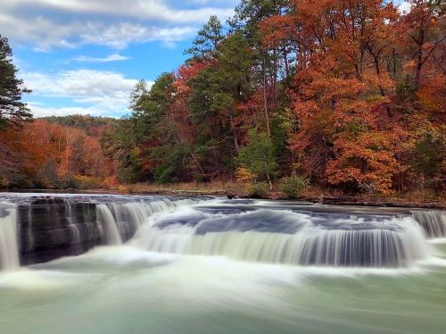 A serene waterfall surrounded by vibrant autumn foliage and a clear blue sky.