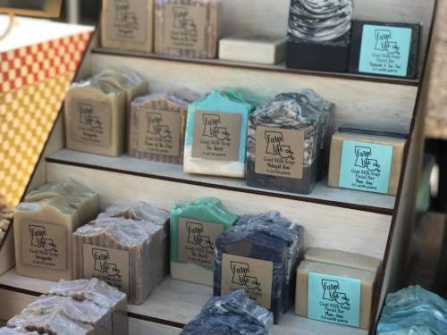 A display of various handmade soaps in different colors and textures arranged on wooden shelves.