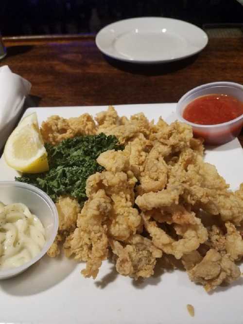 A plate of fried calamari with lemon, kale, and two dipping sauces: one red and one white.