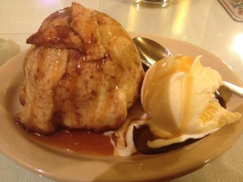 A warm cinnamon apple dumpling drizzled with caramel sauce, served with a scoop of vanilla ice cream on the side.