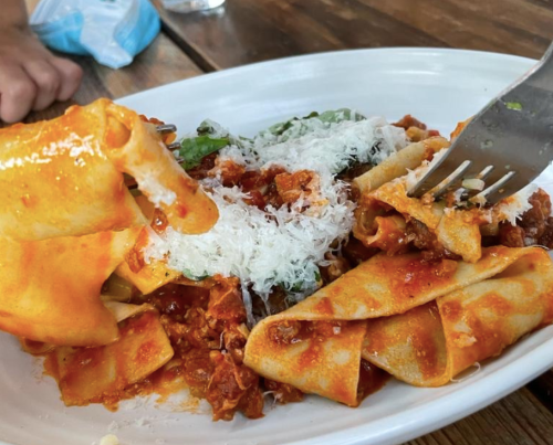 A plate of pasta topped with meat sauce and grated cheese, with a fork lifting a piece of pasta.