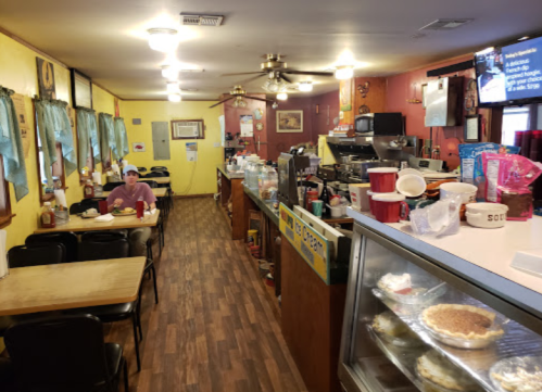 A cozy diner interior with a counter, tables, and a customer eating. The decor includes colorful walls and a TV.