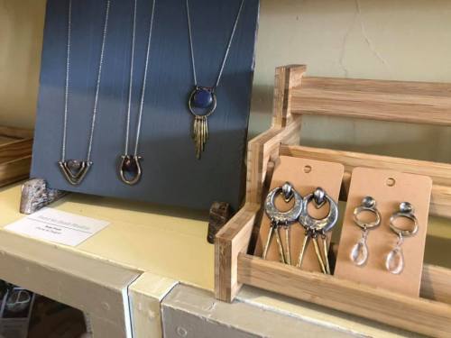 Display of handmade jewelry featuring necklaces and earrings on a wooden stand.