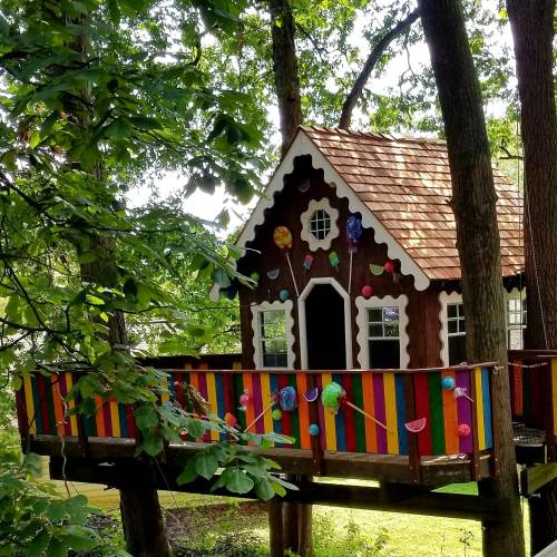 A whimsical treehouse with colorful decorations and a vibrant railing, nestled among green trees.