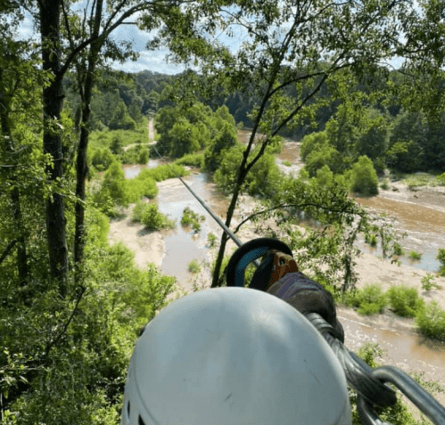 A view from above showing a river winding through lush greenery, with a safety harness and helmet in the foreground.
