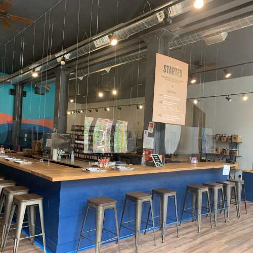 A modern café interior featuring a wooden bar, metal stools, and a menu board on the wall. Bright and inviting atmosphere.