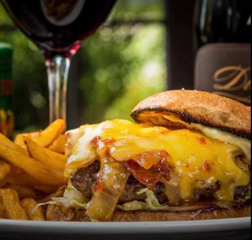 A juicy cheeseburger with melted cheese, lettuce, and bacon, served with fries and a glass of red wine.