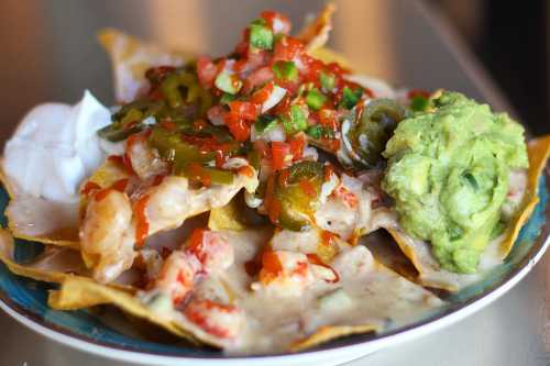 A plate of nachos topped with cheese, jalapeños, salsa, guacamole, and sour cream.