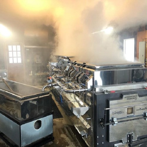 A stainless steel machine in a foggy, steamy environment, likely used for cooking or processing food.