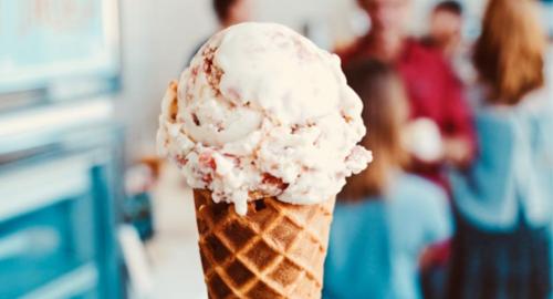 A close-up of a waffle cone filled with creamy ice cream, with people enjoying ice cream in the background.