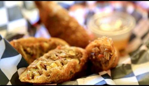 A close-up of crispy fried food with a filling, served in a basket with a small cup of dipping sauce.