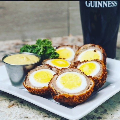 A plate of Scotch eggs with a side of mustard and a pint of Guinness in the background.