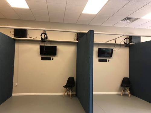 Two separate rooms with blue partitions, each containing a chair and a wall-mounted TV.
