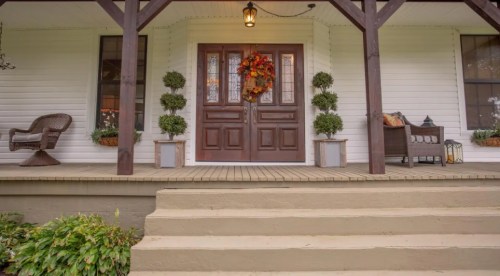 A welcoming front porch with a wooden door, seasonal wreath, potted plants, and cozy seating.
