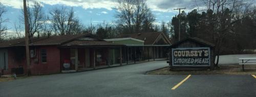 A small building with a sign reading "Courtsy's Smoked Meats," surrounded by trees and a parking area.