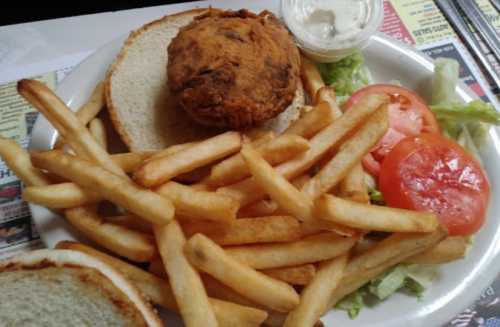 A plate with a fried chicken sandwich, lettuce, tomato slices, and a side of golden French fries.