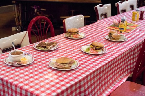 A table with a red and white checkered tablecloth featuring several burgers, a plate of fries, and condiments.