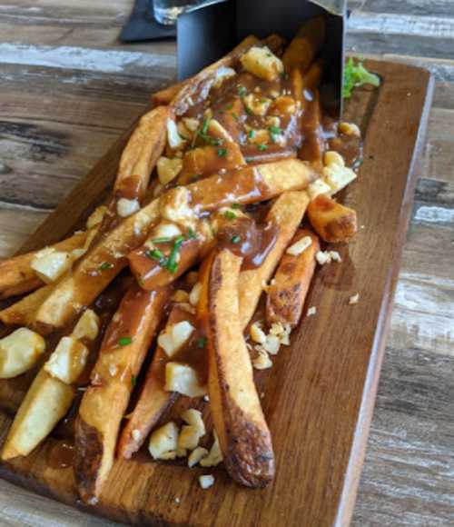 A wooden platter with crispy fries topped with gravy and cheese curds, served in a metal container.