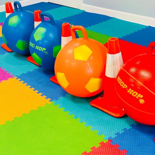 Colorful play area with blue and orange soccer balls and traffic cones on a vibrant foam mat.