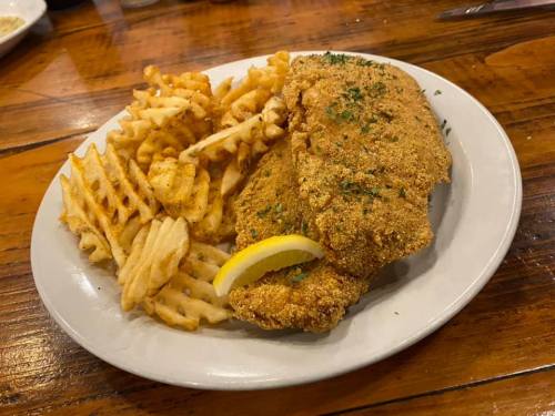 A plate of golden-brown fried fish with a lemon wedge, served alongside crispy waffle fries.