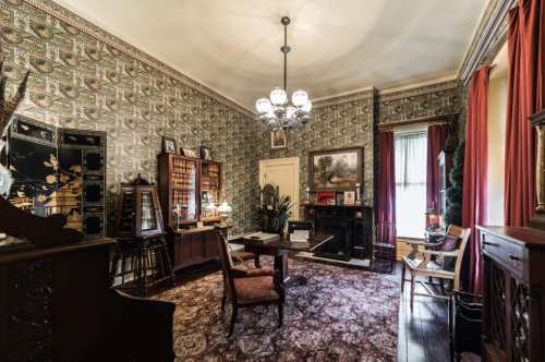 A vintage office with patterned wallpaper, a chandelier, wooden furniture, and a cozy atmosphere.