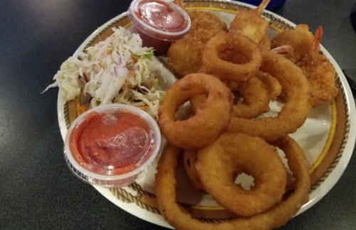A plate of fried shrimp, onion rings, coleslaw, and two cups of dipping sauce.