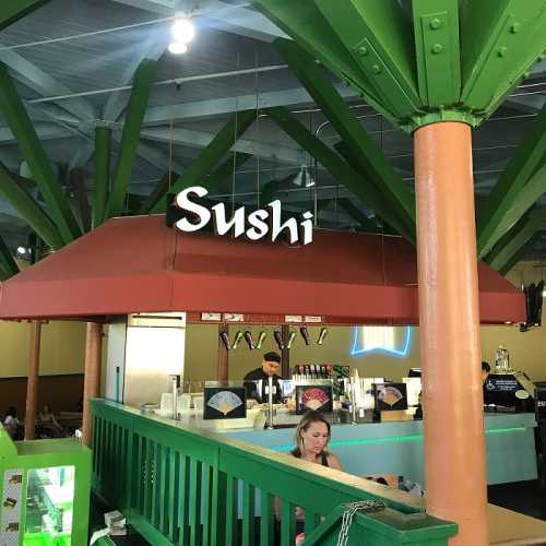 A colorful sushi restaurant with a prominent sign and a woman sitting at a green railing.