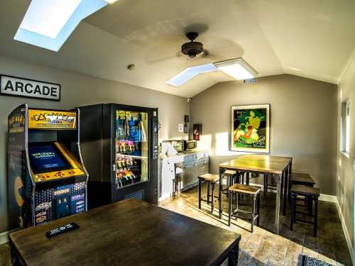 A bright game room featuring arcade machines, a vending machine, and wooden tables with chairs.