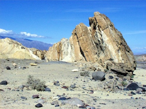 Rocky formations rise from a sandy landscape under a clear blue sky, with distant mountains in the background.