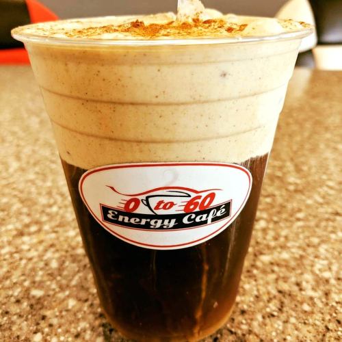 A layered iced coffee drink in a clear cup, topped with whipped cream and a sprinkle of cinnamon.